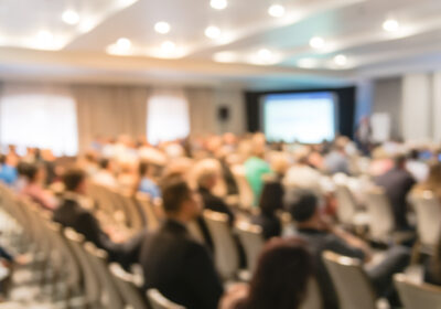 Réunion de séminaire d'entreprise floue avec écran LED projecteur et discours de conférencier sur scène. Audience rétrovisée défocalisée dans la salle de conférence.