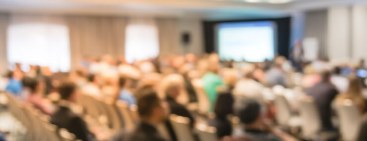 Réunion de séminaire d'entreprise floue avec écran LED projecteur et discours de conférencier sur scène. Audience rétrovisée défocalisée dans la salle de conférence.